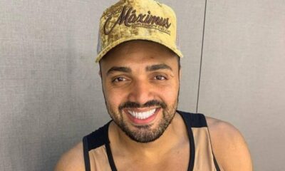 Homem sorridente com barba, bigode e boné dourado escrito "Circo Maximus" olhando para frente