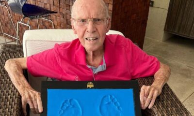 Homem idoso de óculos e camisa rosa segura quadro com pegadas azuis de bebê