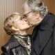Mulher idosa de óculos e cabelo loiro curto beijando homem idoso de óculos e cabelo grisalho