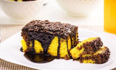 Fatia de bolo de cenoura amarelo com cobertura de chocolate escuro e granulado em prato branco