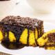 Fatia de bolo de cenoura amarelo com cobertura de chocolate escuro e granulado em prato branco