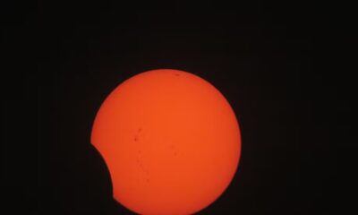 Sol laranja com manchas escuras, parcialmente coberto por um objeto circular escuro