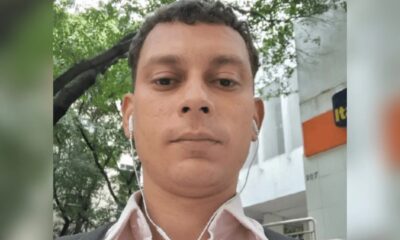 Homem com fones de ouvido brancos, em frente a edifício com as letras 'It' e '207'