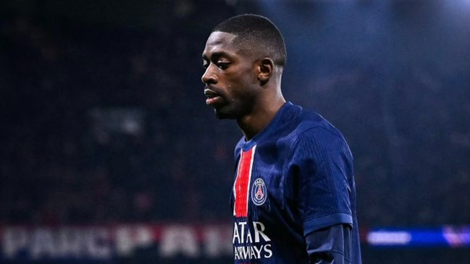 Jogador Ousmane Dembélé em camisa azul do PSG com listra vermelha