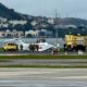 Avião branco fora da pista, cercado por bombeiros e veículos de emergência em aeroporto costeiro