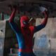 Homem-Aranha com traje vermelho e azul, erguendo grande objeto metálico acima da cabeça