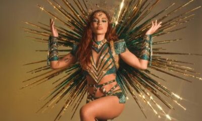 Cantora Anitta em fantasia dourada e verde com coroa e fundo de raios brilhantes