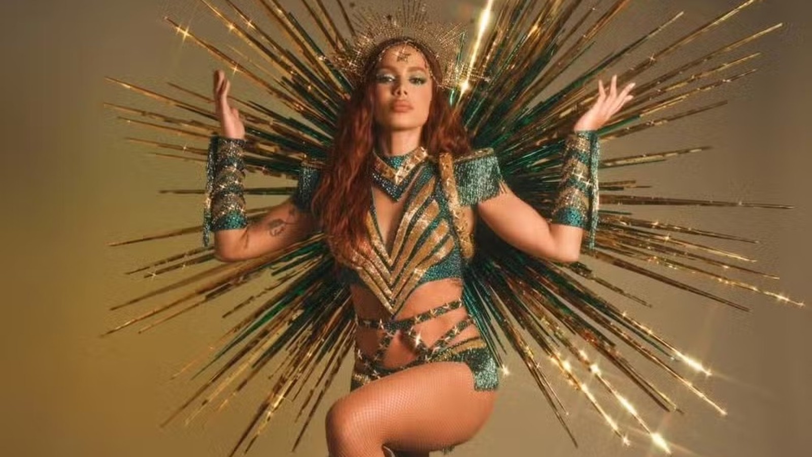 Cantora Anitta em fantasia dourada e verde com coroa e fundo de raios brilhantes