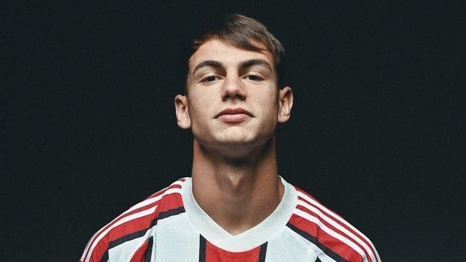 Retrato de homem jovem com cabelo escuro vestindo camisa listrada de futebol
