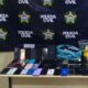 Dezenas de celulares e caixas sobre uma mesa, com um banner da Polícia Civil ao fundo