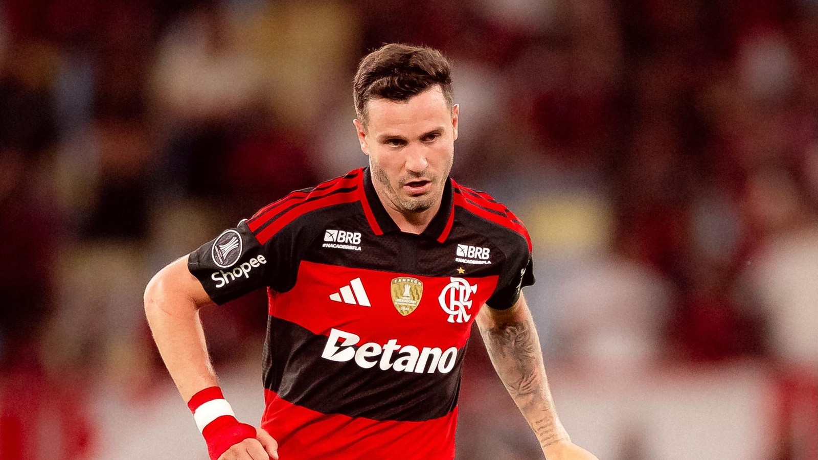 Saúl Níguez, jogador do Flamengo, em campo, camisa vermelha e preta, olhar sério