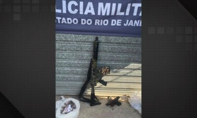 Fuzil camuflado, duas pistolas, sacolas com entorpecentes e banner da Polícia Militar