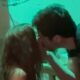 Homem e mulher se beijam, com luz teal no fundo