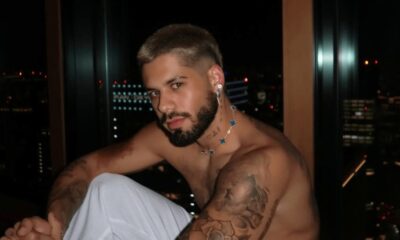 Zé Felipe sem camisa, com barba e colar, vista noturna ao fundo