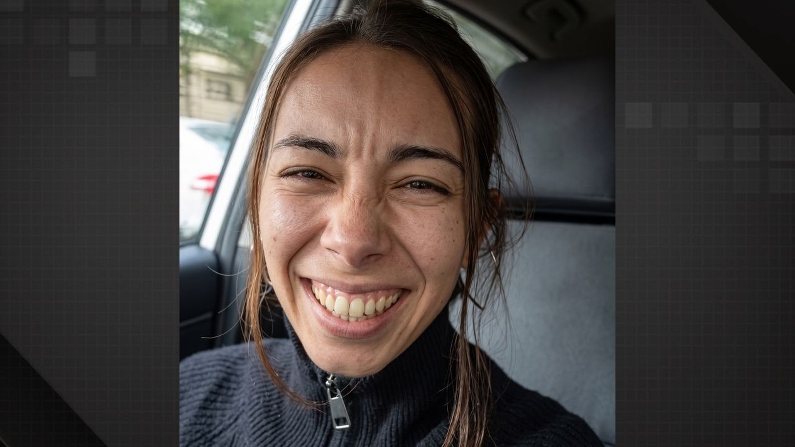 Mulher de cabelos castanhos rindo intensamente com olhos apertados dentro de um carro