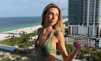 Mulher loira sorrindo na varanda com vista para praia e cidade