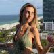Mulher loira sorrindo na varanda com vista para praia e cidade