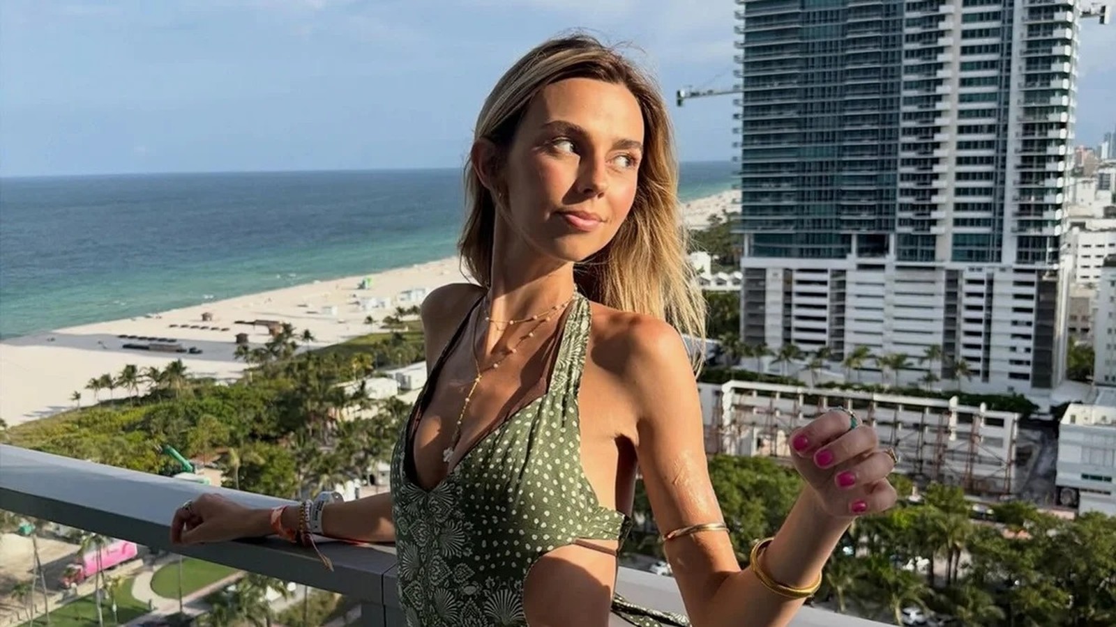 Mulher loira sorrindo na varanda com vista para praia e cidade