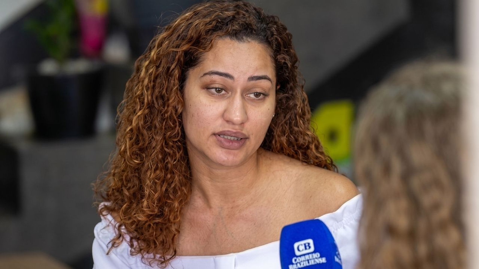 Emiliane Tamara Nunes Carvalho, mulher de cabelos cacheados, fala durante entrevista. Microfone Correio Braziliense.