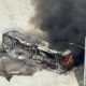 Visão aérea de ônibus carbonizado em chamas com fumaça escura e dois bombeiros o combatendo