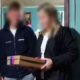 Duas pessoas borradas, homem e mulher, segurando uma caixa marrom com fita rosa e azul em uma porta