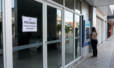 Agência bancária fechada com placa informando o feriado estadual de 5 de agosto e caixa eletrônico disponível ao lado