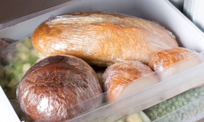Pães diversos, como baguete e pães redondos, embrulhados em plástico, em uma gaveta de freezer