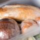 Pães diversos, como baguete e pães redondos, embrulhados em plástico, em uma gaveta de freezer