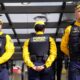 Três guardas municipais em uniforme amarelo e azul com coletes pretos e boinas amarelas em formação