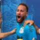 Jogador Neymar com boca aberta, camisa azul de futebol, braços de duas pessoas