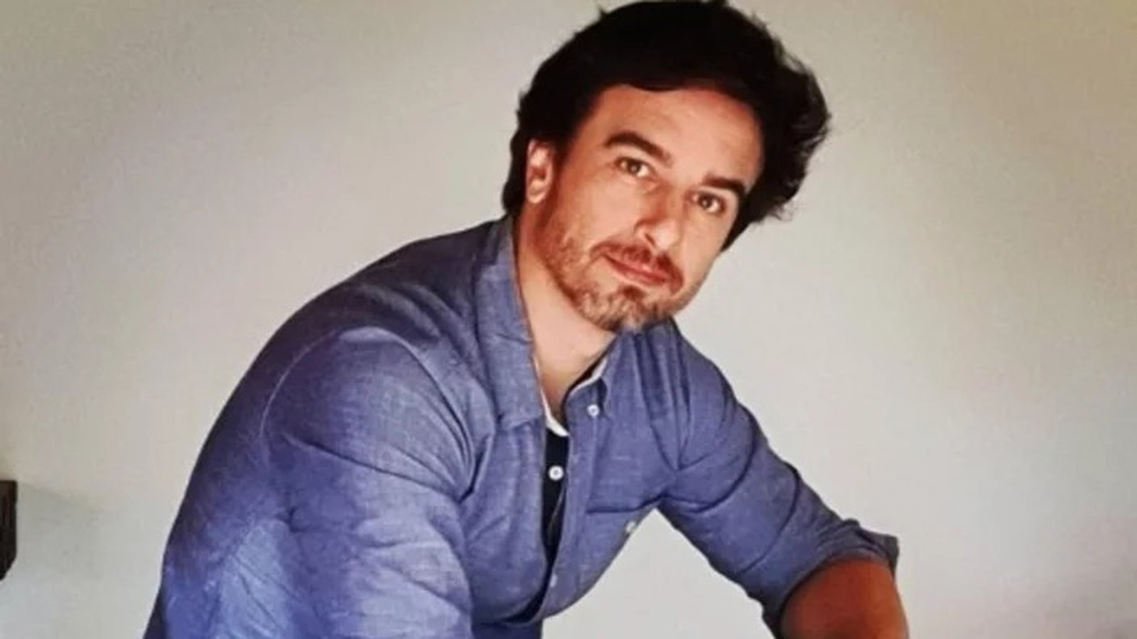 Homem de cabelo e barba escura, camisa azul, olhando para câmera