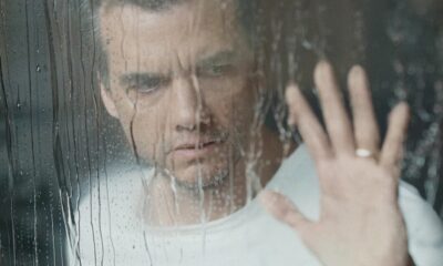Homem sério através de vidro com chuva, sua mão com anel toca a superfície