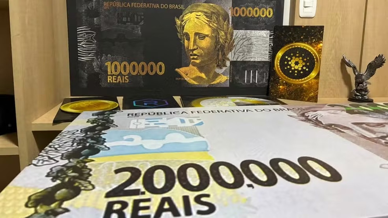 Notas decorativas de 1.000.000 e 2.000.000 Reais, logo Cardano, e estatueta de águia