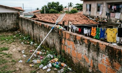 Terreno com lixo acumulado ao lado de um muro de tijolos e rede de piscina