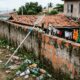 Terreno com lixo acumulado ao lado de um muro de tijolos e rede de piscina