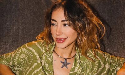 Mulher com cabelo castanho ondulado e camisa verde estampada usando colar com estrela-do-mar
