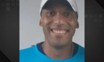Close-up de homem negro sorrindo, usando boné branco e camiseta azul