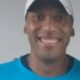 Close-up de homem negro sorrindo, usando boné branco e camiseta azul
