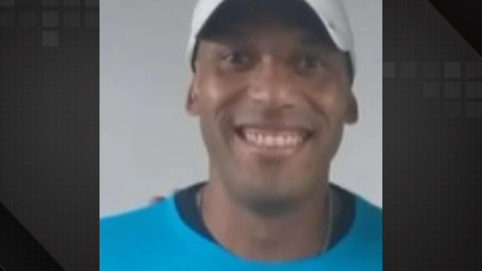 Close-up de homem negro sorrindo, usando boné branco e camiseta azul