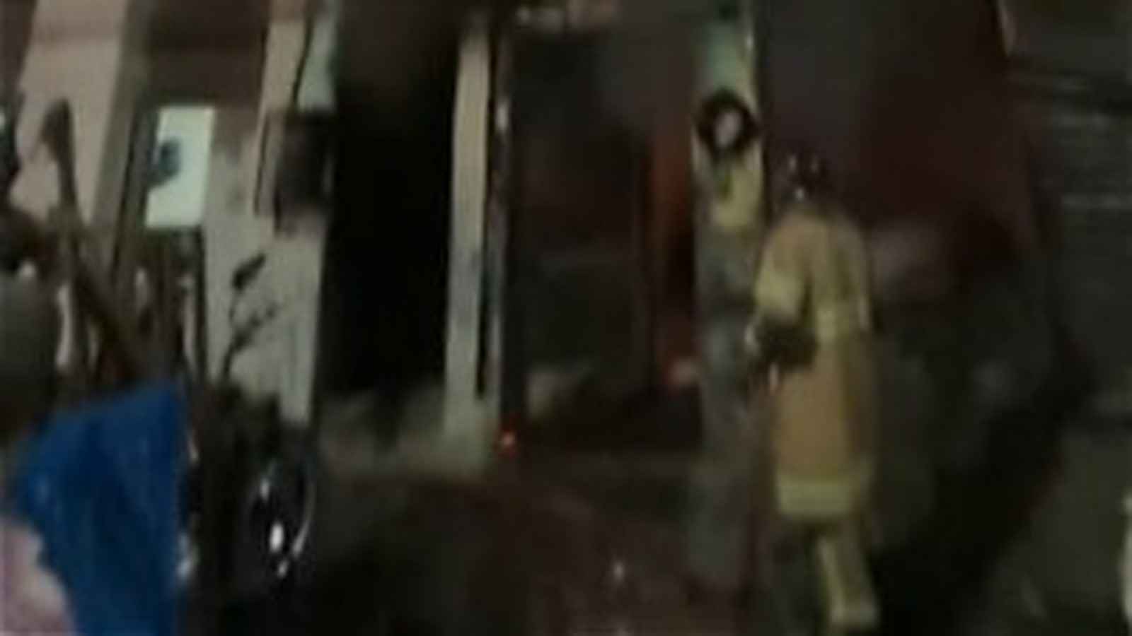 Bombeiro em uniforme amarelo caminha em área escura de prédio após incêndio