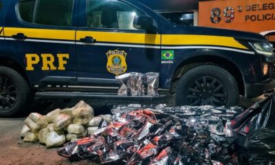 Veículo da PRF e grande quantidade de pacotes de drogas, alguns metálicos, outros em plástico, no chão.