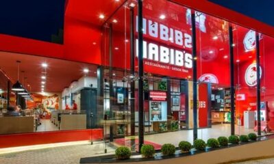 Restaurante Habib's com fachada vermelha, nome em branco, janelas de vidro, interior iluminado, pessoas