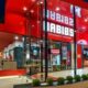 Restaurante Habib's com fachada vermelha, nome em branco, janelas de vidro, interior iluminado, pessoas