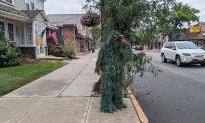 Pessoa com roupa de camuflagem de arbusto e binóculos na calçada de rua urbana