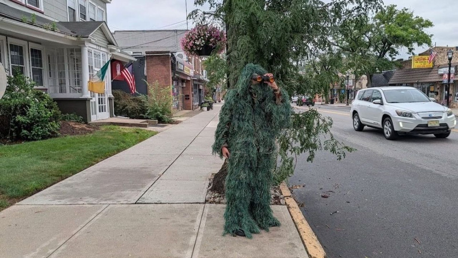 Pessoa com roupa de camuflagem de arbusto e binóculos na calçada de rua urbana