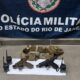 Duas pistolas, dois rádios e cinto tático sobre o chão com banner da Polícia Militar