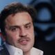 Homem, Pablo Marçal, de terno, camisa branca e bigode, em fundo desfocado azul