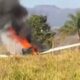 Pequeno avião em chamas com fumaça preta em campo de grama e árvores