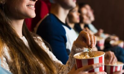 Mulher sorridente segura balde de pipoca em cinema, com outros espectadores assistindo ao fundo