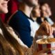 Mulher sorridente segura balde de pipoca em cinema, com outros espectadores assistindo ao fundo
